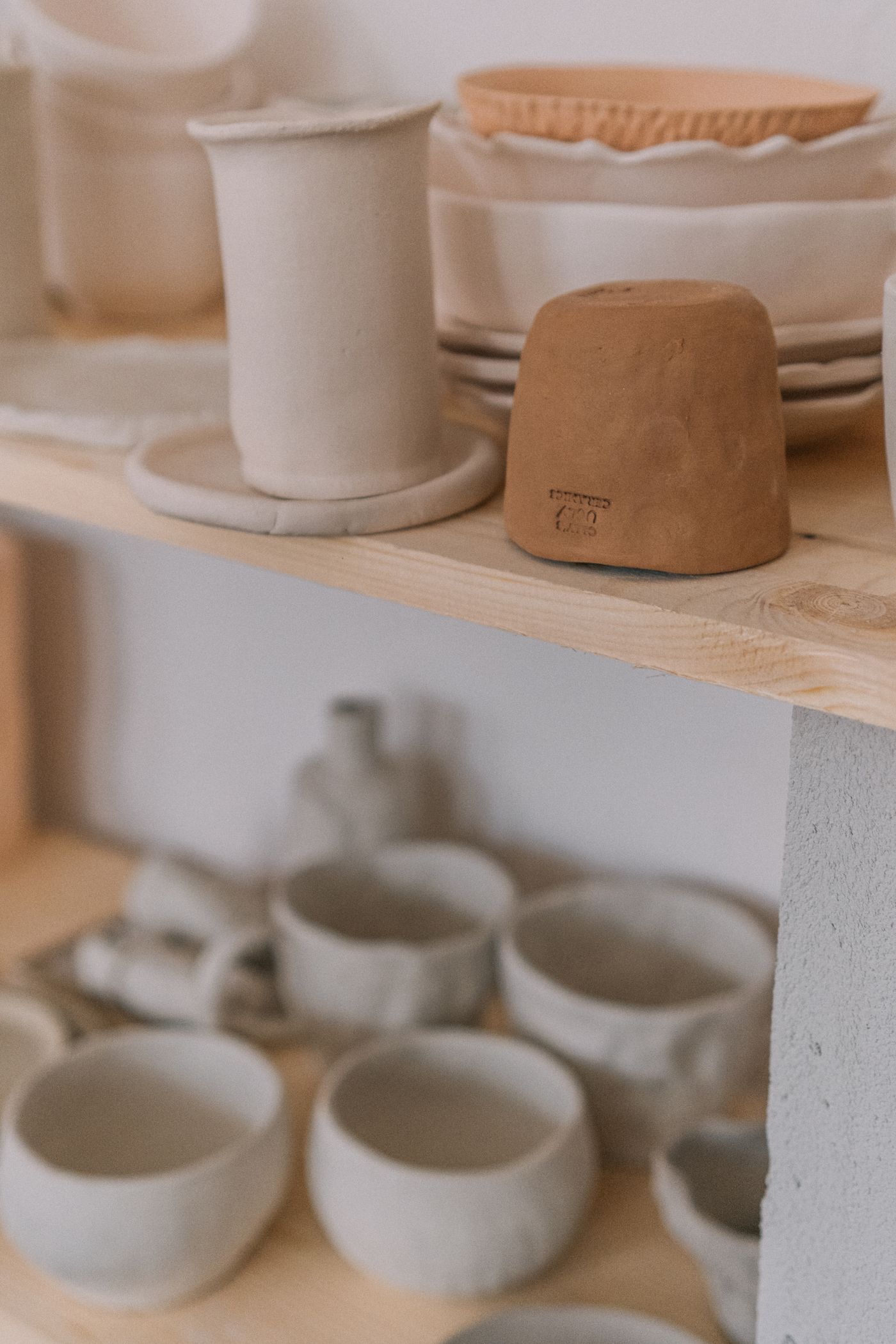 Handmade cups and bowls on a wooden studio shelf